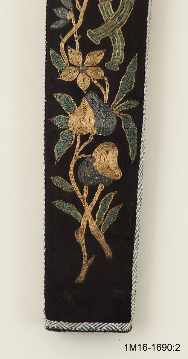 FODRAL TILL SOLFJÄDER. SVART SIDEN SPÄND ÖVER BRUN PAPP MED BLOMBRODERIER AV GULD- OCH SILVERTRÅD. KANTAD MED BLÅTT OCH VITT SIDENBAND. FODRAD MED LJUSBLÅTT SIDEN. GRÅBRUNT BAND ATT BÄRA I, MED TVÅ GRÖNA OVALA GLASSTENAR.
