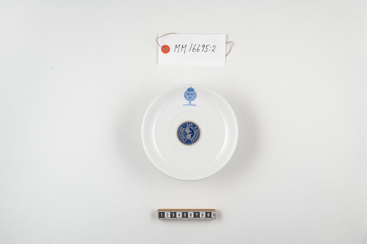 Cylindriskt fat i vitt porslin. Dekorerat med lilla riksvapnet samt därunder texten: " H M Sverige ". Dekoren utfört i blått. På undersidan stämplat i blått: Rörstrand. Dessutom ett påklistrat munlack i blått med vit text enligt följande: Karl Björkmans Jern-Glas- & Porslinshandel Ronnebygatan 36 Karlskrona.