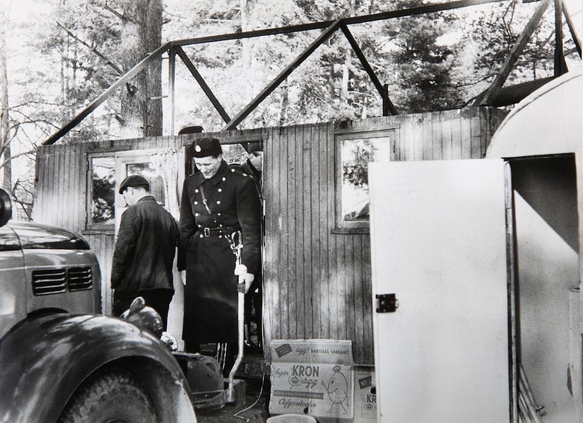 Bilden är troligen tagen i samband med en vräkning av romer i Lilla Sköndal, Stockholm år 1959. Vid Lilla Sköndal har romska boplatser i olika former funnits åtminstone sedan år 1943, då staden iordningsställde en lägerplats. Lägret låg då vid en bergsknalle vid Skogskyrkogårdens södra del och år 1944 bodde här ett trettiotal personer. De boende fick hämta vatten hos några boende i närheten.