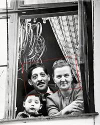 Ur ett fönster tittar ett gift par och deras lille son ut. E