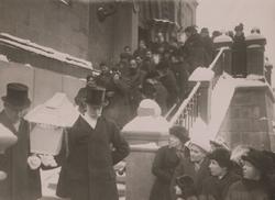 Ett begravningsfölje tågar nedför en kyrktrappa. Under 1900-