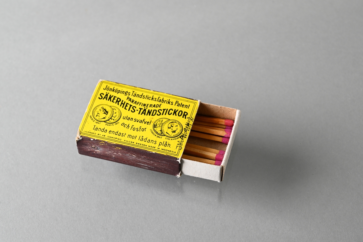 Tändsticksask bestående av innerask och ytterask. Ytteraskens ovansida är gul och har tryckt text: "Jönköpings Tändsticksfabriks Patent PARAFFINERADE SÄKERHETS-TÄNDSTICKOR utan svafvel och fosfor Tänd endast mot lådans plån LICENSED BY AB JÖNKÖPING-VULCAN SWEDEN MADE IN INDONESIA". På ytteraskens ovansida finns även tryckta bilder av medaljer från utställningar i Paris 1855 och 1867, och utställningar i London 1862 och Stockholm 1866. Ytteraskens undersida är blå. Asken innehåller nio oanvända tändstickor.

JM 41914:1, innerask
JM 41914:2, ytterask