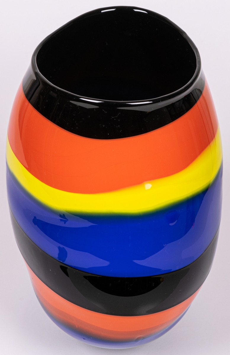 Vas, blåst, med pålagda färgfält, modell "Mali". Oregelbundet oval, bukig i längdled. Tvärrandig i svart, orange, gult och blått. Avrundad mot smal, tjock fot. Märkt under: "Utställning".