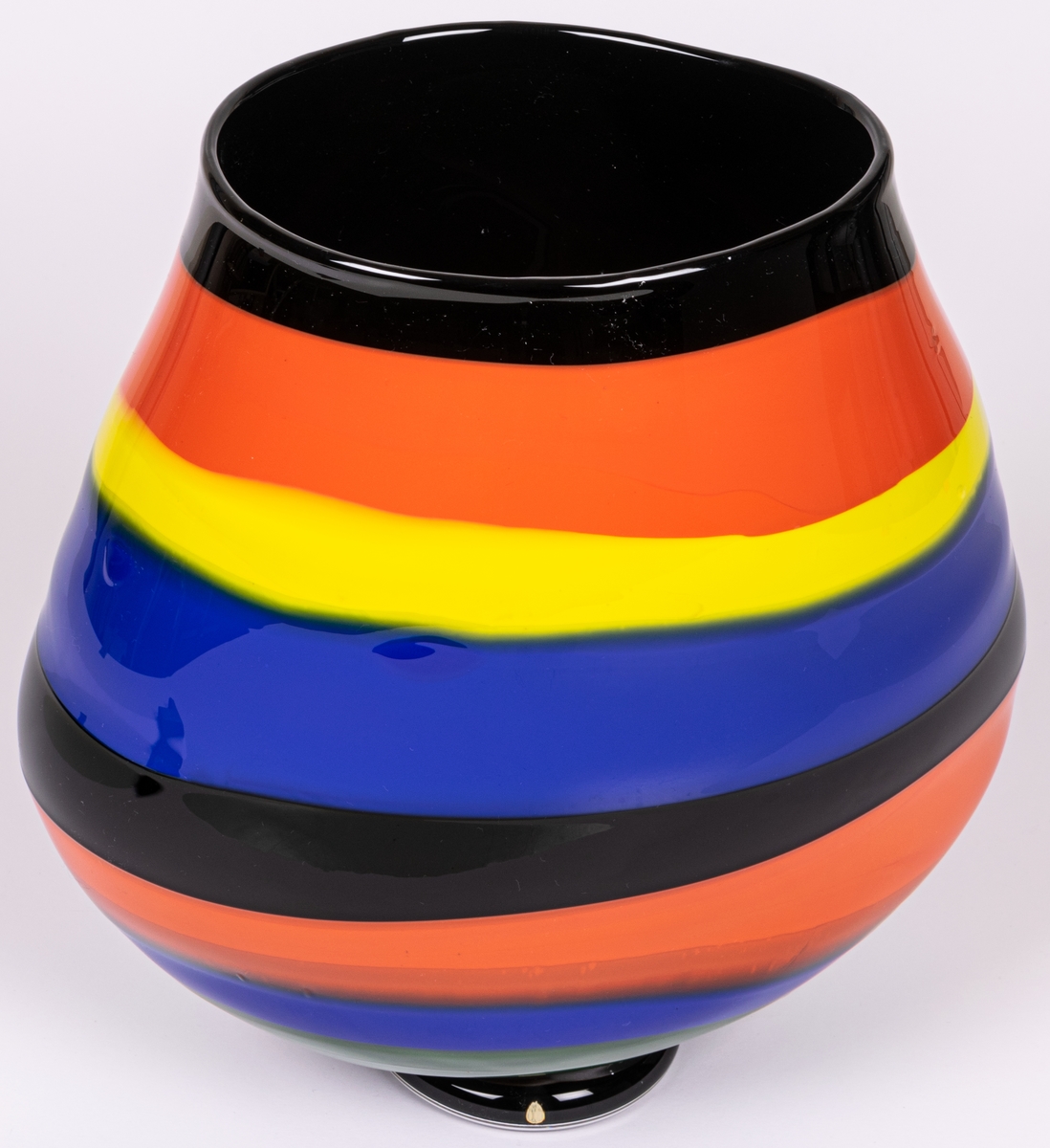 Vas, blåst, med pålagda färgfält, modell "Mali". Oregelbundet oval, bukig i längdled. Tvärrandig i svart, orange, gult och blått. Avrundad mot smal, tjock fot. Märkt under: "Utställning".