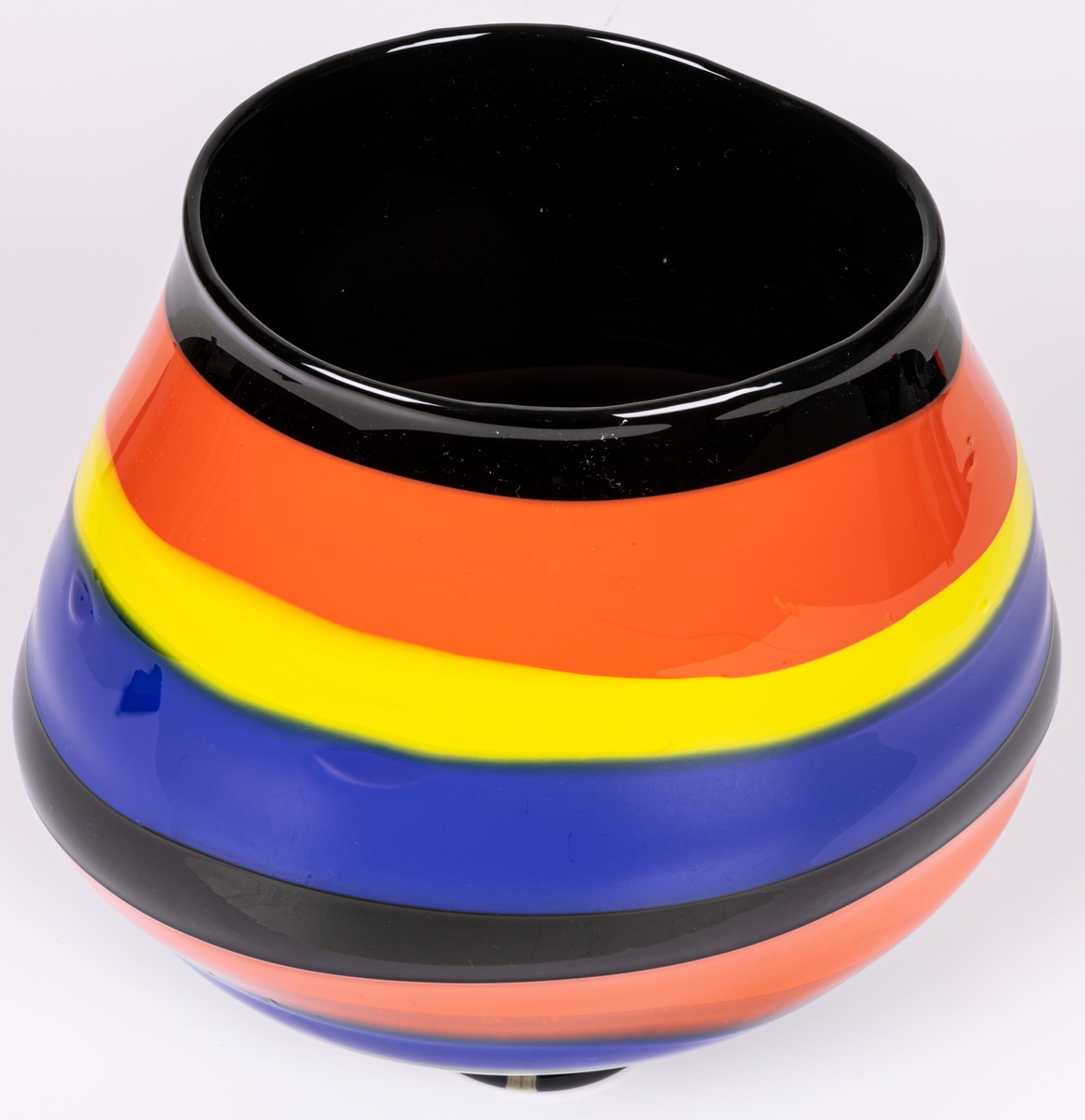 Vas, blåst, med pålagda färgfält, modell "Mali". Oregelbundet oval, bukig i längdled. Tvärrandig i svart, orange, gult och blått. Avrundad mot smal, tjock fot. Märkt under: "Utställning".