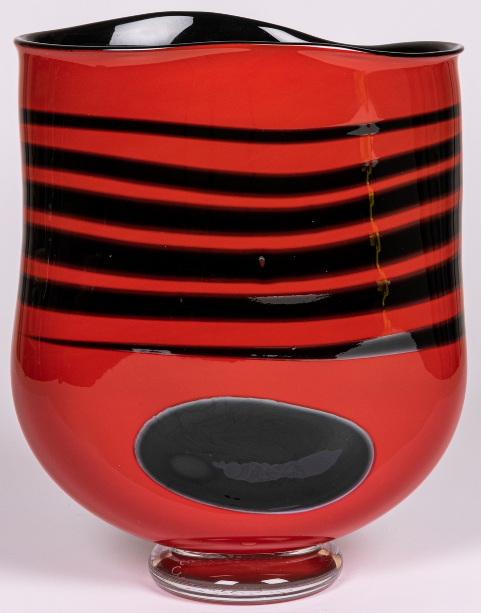 Vas, blåst, med pålagda färgfält, modell "Mali". Tillplattat oval. Röd med sex svarta tvärränder ovan en svart oval. Rundad nedtill mot smal, ofärgad fot.