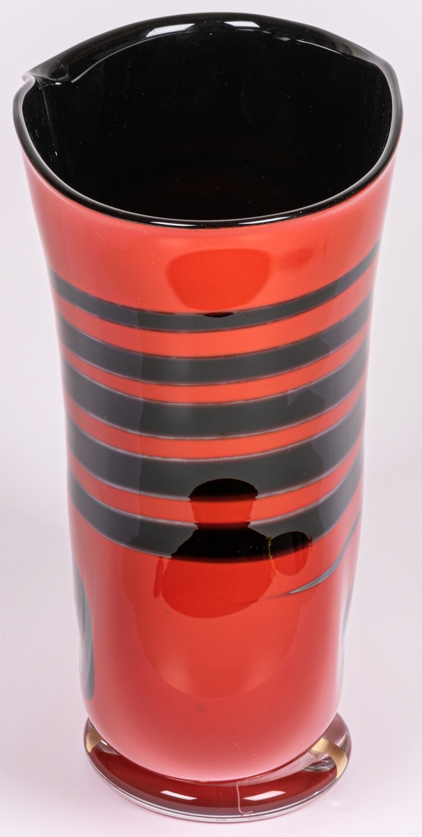 Vas, blåst, med pålagda färgfält, modell "Mali". Tillplattat oval. Röd med sex svarta tvärränder ovan en svart oval. Rundad nedtill mot smal, ofärgad fot.