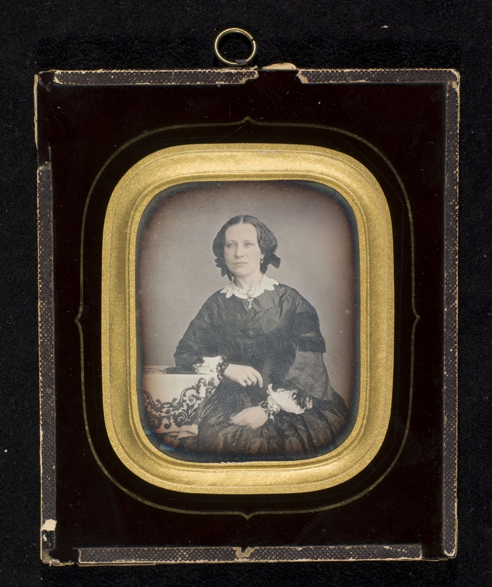 Daguerreotypi av kvinne som sitter ved et bord.