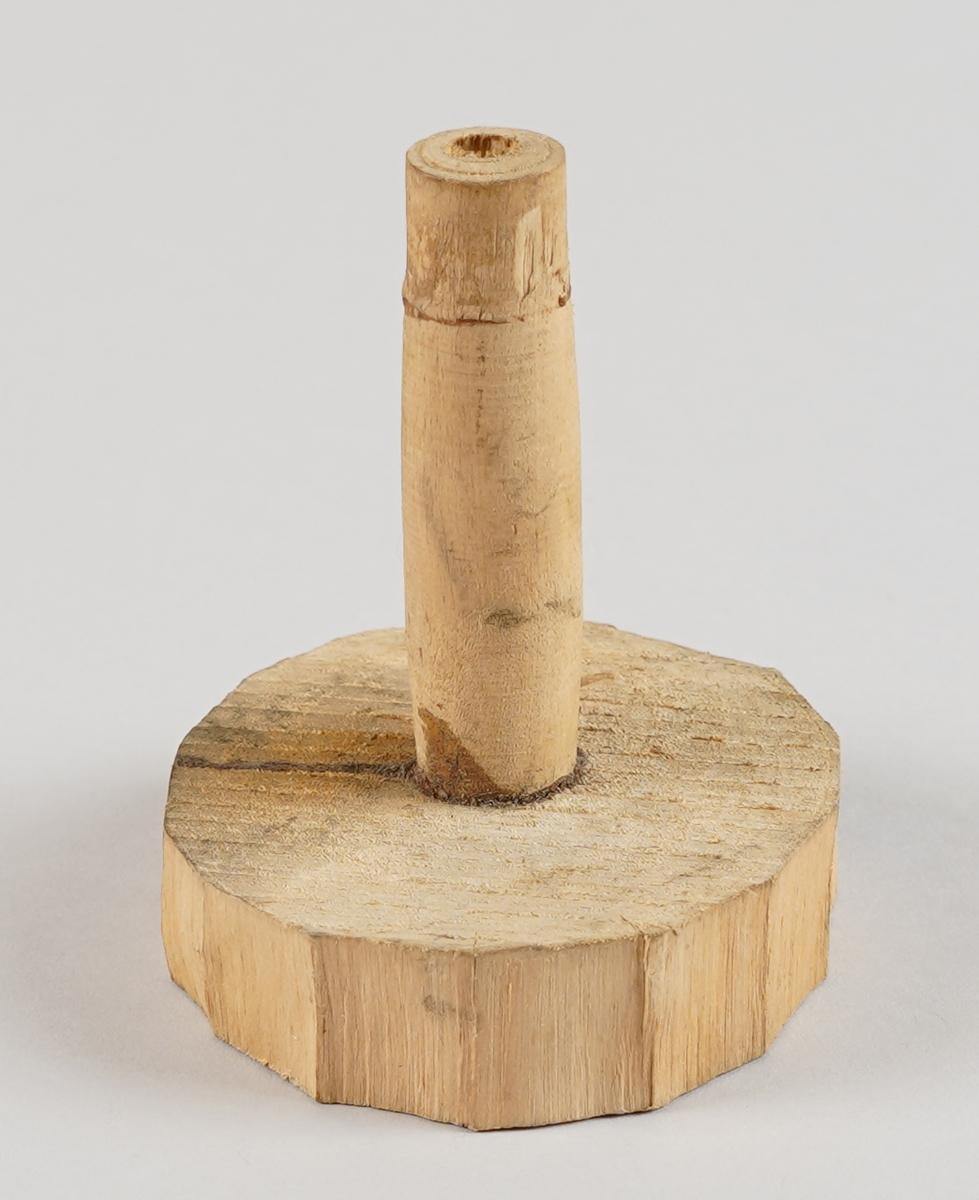 Emne til snelle (som er del av tein til hjulrokk) der eine klossen er borte.  Eit dreia stykkje er sett ned i ein tilnærma sirkelforma kloss i eine enda. Det er hol gjennom dei to delane i senter.