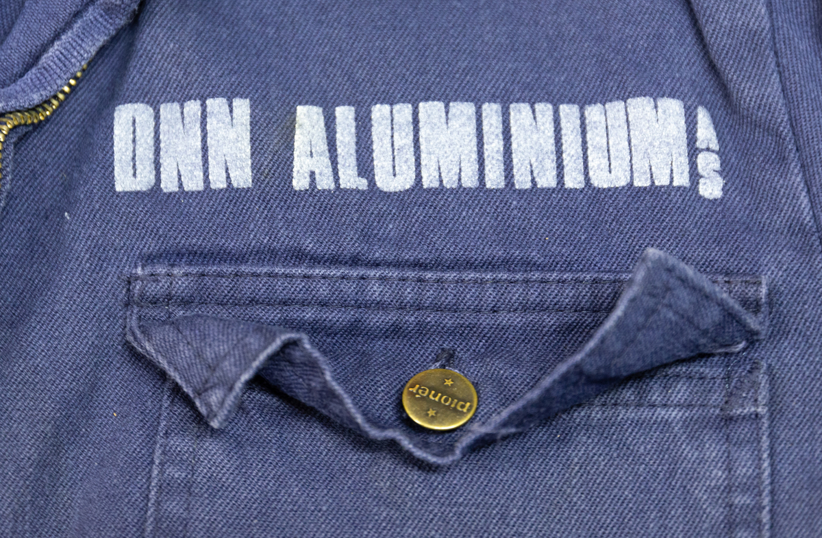 Todelt dress i mørk blå bomullsdenim. Storleik 48 (båe delene). Glidelås i metall framme i jakke, knepping med metallknappar i buksegylf. To brystlommer på jakka, to stikklommer i buksa. Innside av bukselinning i tynt nylonstoff (?). Buksa har produsentmerket laminert fast i høgre lomme og jakka har tilsvarande på innsida bak høgre brystlomme. Vaskeanvisning 60 gr. 

Buksa har fleire større og mindre hol, særleg nede på venstre buksebein, - både framme og bak. Om desse er forårsaka av varme eller syre er ikkje kartlagt, men fargen tyder på høg varme. Det er ikkje gjort forsøk på reparasjon av hola. Stoffet er ikkje flammehemma.