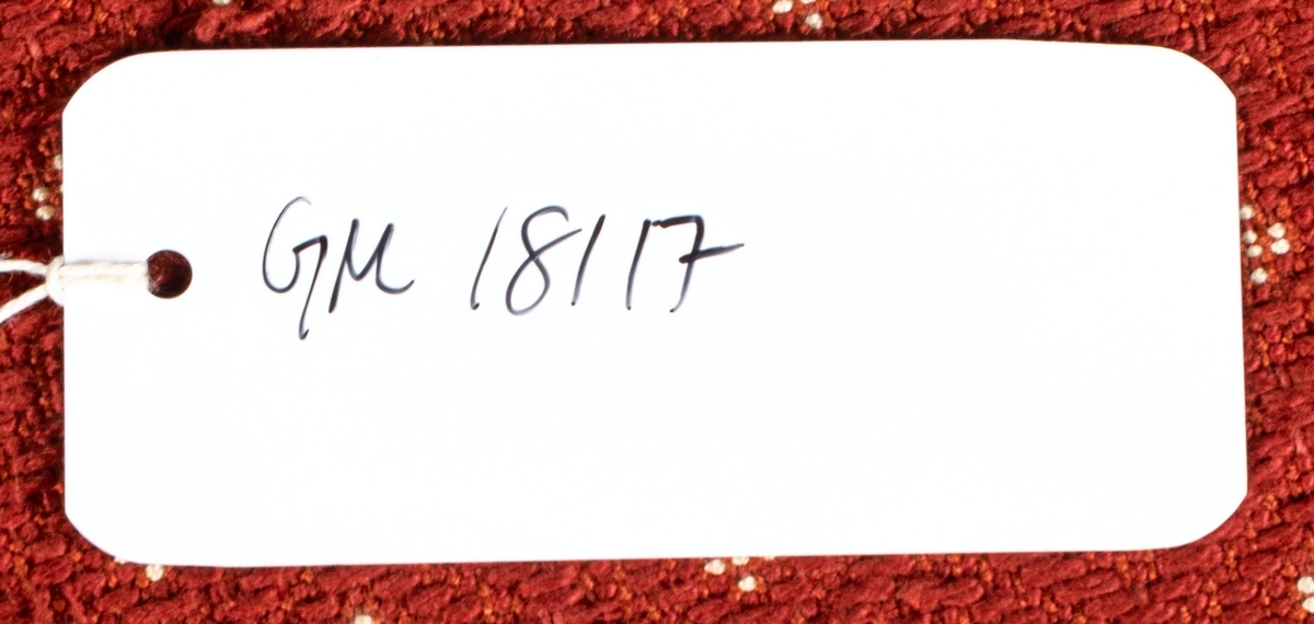 Katalogkort: Fåtölj. Ljust träslag i armstöd och ben. Sits och ryggstöd klädda med mönstervävt tyg. Varp: röd. Inslag: rett, vitt. Gåsögonliknande mönster. Sitsens kant, kantad med snodd i rött och vitt. På stolsryggens framsida fanns ursprungligen 3 textilklädda knappar, varav en saknas.

h 80cm, b 66cm, dj 77cm