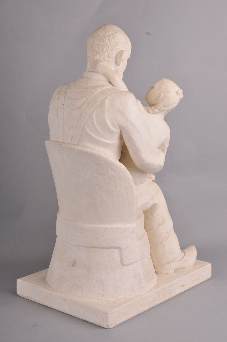 Gamal mann med heilskjegg. Mannen sit i ein kubbestol og har tresko på føtane. Ein berrføtt jentunge med fletta hår sit på fanget og ser bestefaren i andletet. Tittel: "Bestefar fortel."