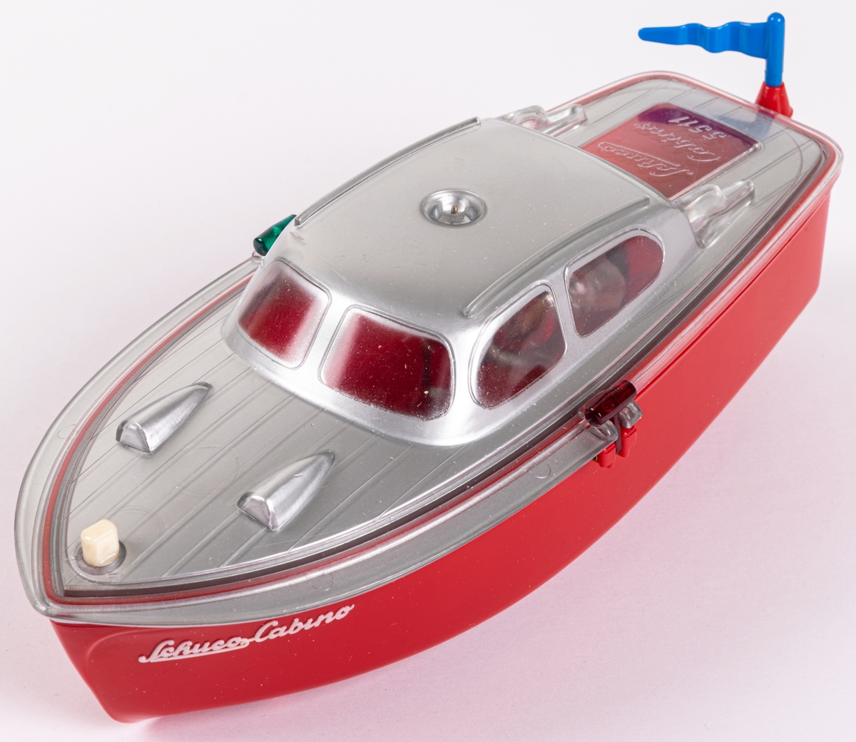 Leksaksbåt av gjuten hårdplast. Rött skrov och grått däckparti. Drivs med batteri. Ett batteri finns kvar. Båten ligger i orginalförpackning med bruksanvisning på engelska. Modell Cabino 5511. Tillverkad av Schuco i Tyskland.