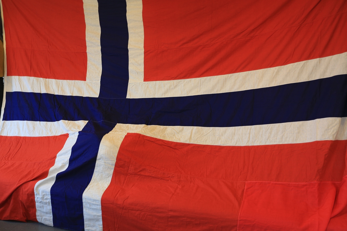 Norsk flagg. Reparert med tøy i annen rødnyanse i det ene hjørnet.