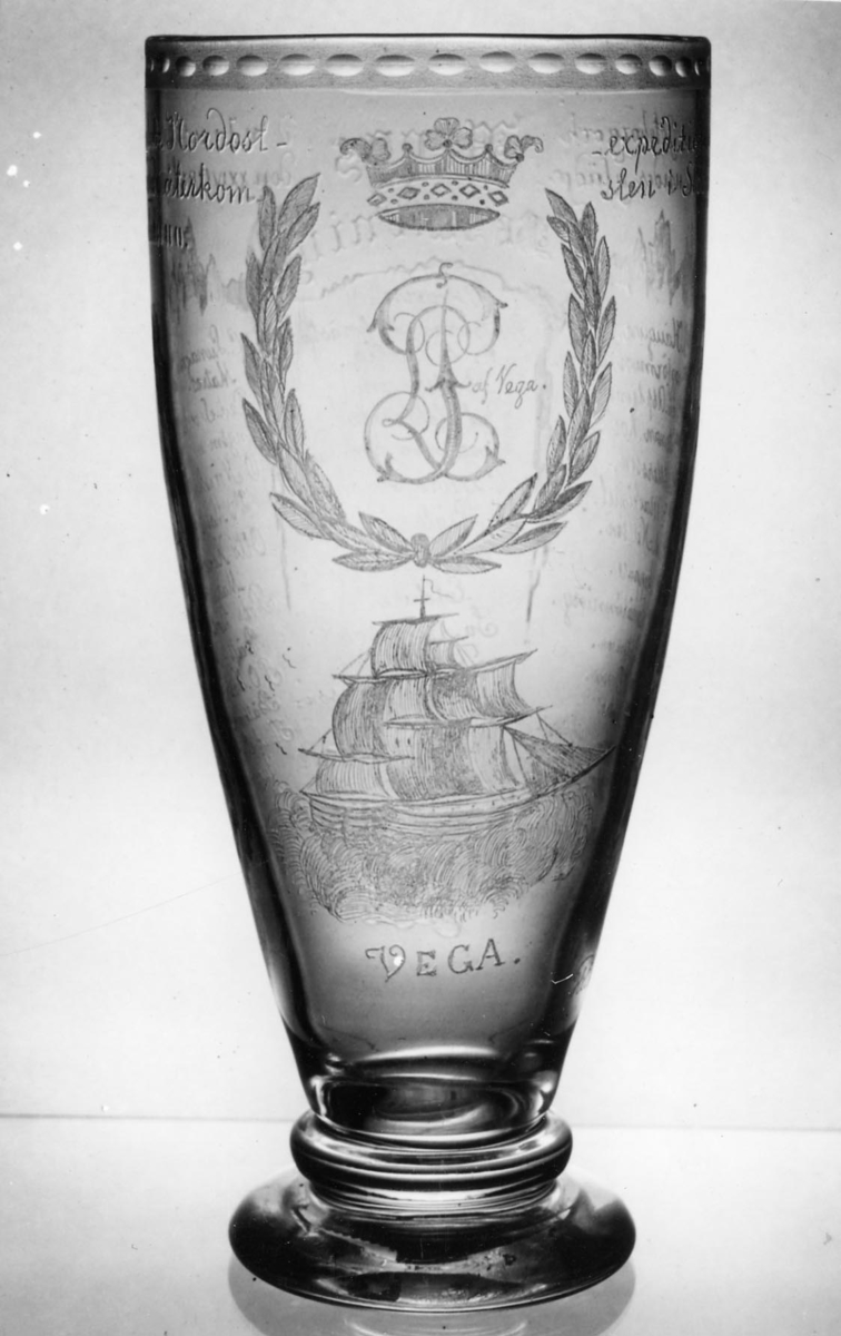 Minnespokal över Vegaexpeditionen 1879. Etsat, slipat glas med Vegas bild och ett ankare samt Louis Palander af Vegas monogram inom bladdekor. Pokalens kant försedd med etsad pärldekor. Förutom minnestexten överst en förteckning över Vegas besättning.