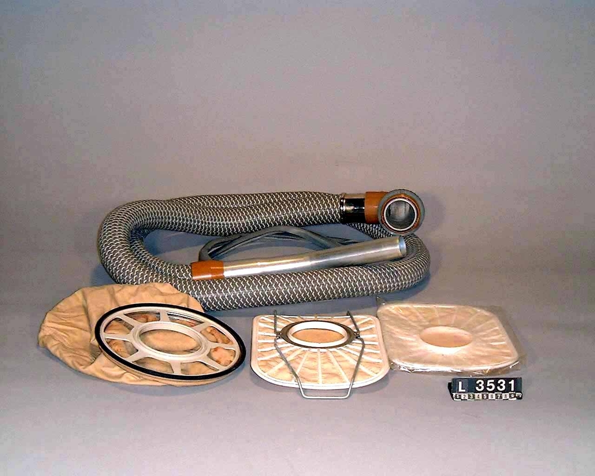 Industri-/hotell- dammsugare med två motorer. Dammsugaren har två strörre hjul på  sidorna och ett mindre styrhjul fram. Apparaten är färgsatt i brunt och vitt.