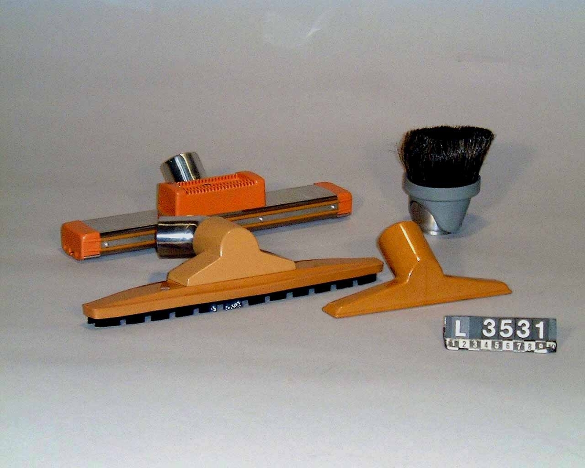 Industri-/hotell- dammsugare med två motorer. Dammsugaren har två strörre hjul på  sidorna och ett mindre styrhjul fram. Apparaten är färgsatt i brunt och vitt.