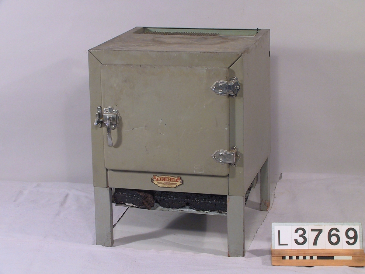 Litet kylskåp i grå/grön metall, absorptionsmodell med utrustning för stadsgas. Under dörren finns en skylt med följande inskription: "Electrolux the gas refrigerator. Made in England."