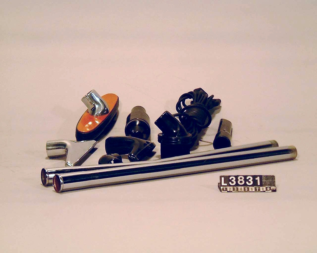 Cylinderdammsugare klädd i vinröd/flammig pegamoid. Fram och bakstycke samt medarna är i metall. Apparaten ligger i en koffert/väska. Under apparaten finns en etikett med Nr 31. Apparaten är alldrig använd, flera av tillbehören är inslagna i papper. Alla delar finns.