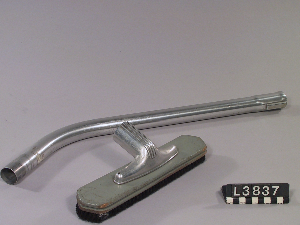 Handdammsugare i blå metallack. Bakstycke i svart bakelit. Skarvrör i aluminum. Golvmunstycke i metall, trä samt med borstring. Svart handtag.