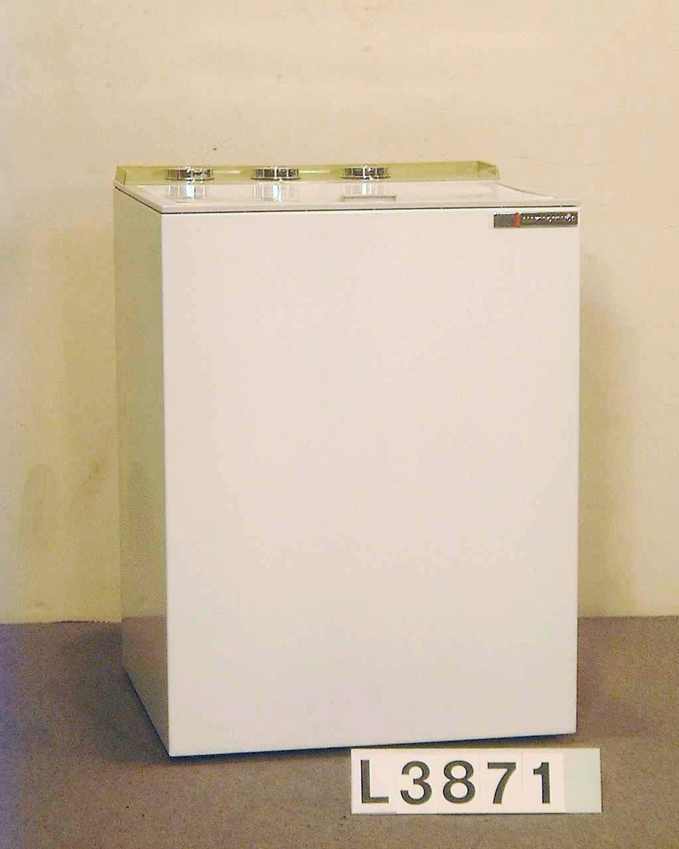 Toppmatad delautomatisk tvättmaskin, maskinen centrifugerar inte. Maskinen är vitlakerad, grå-grön instrumentpanel.  3 st blanka vred samt signallampa. Maskinen kan rullas. Bruksanvisning(kopia) ligger i tvättcylindern. Avloppsslangen har delvis torkat.