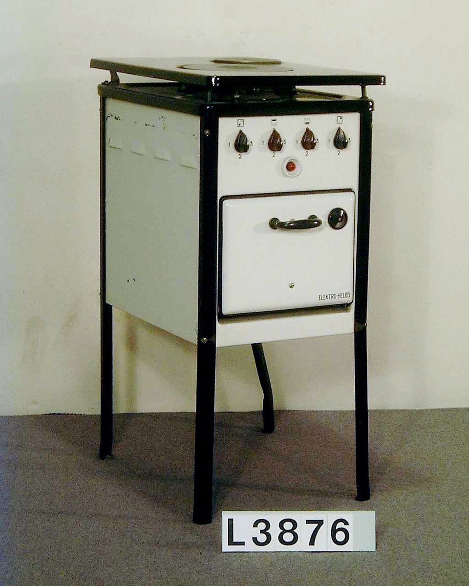 Golvspis på fyra st. svarta emaljerade ben. Två kokplattor, uppfällbar överhäll som är svartemaljerat. Frampartiet och sidorna är vitemaljerade. Ugn, men inget värmeskåp. Strömställarna har tre lägen. Ugnen har ingen termostat, utan två separata vred ett för över och ett för undervärme.