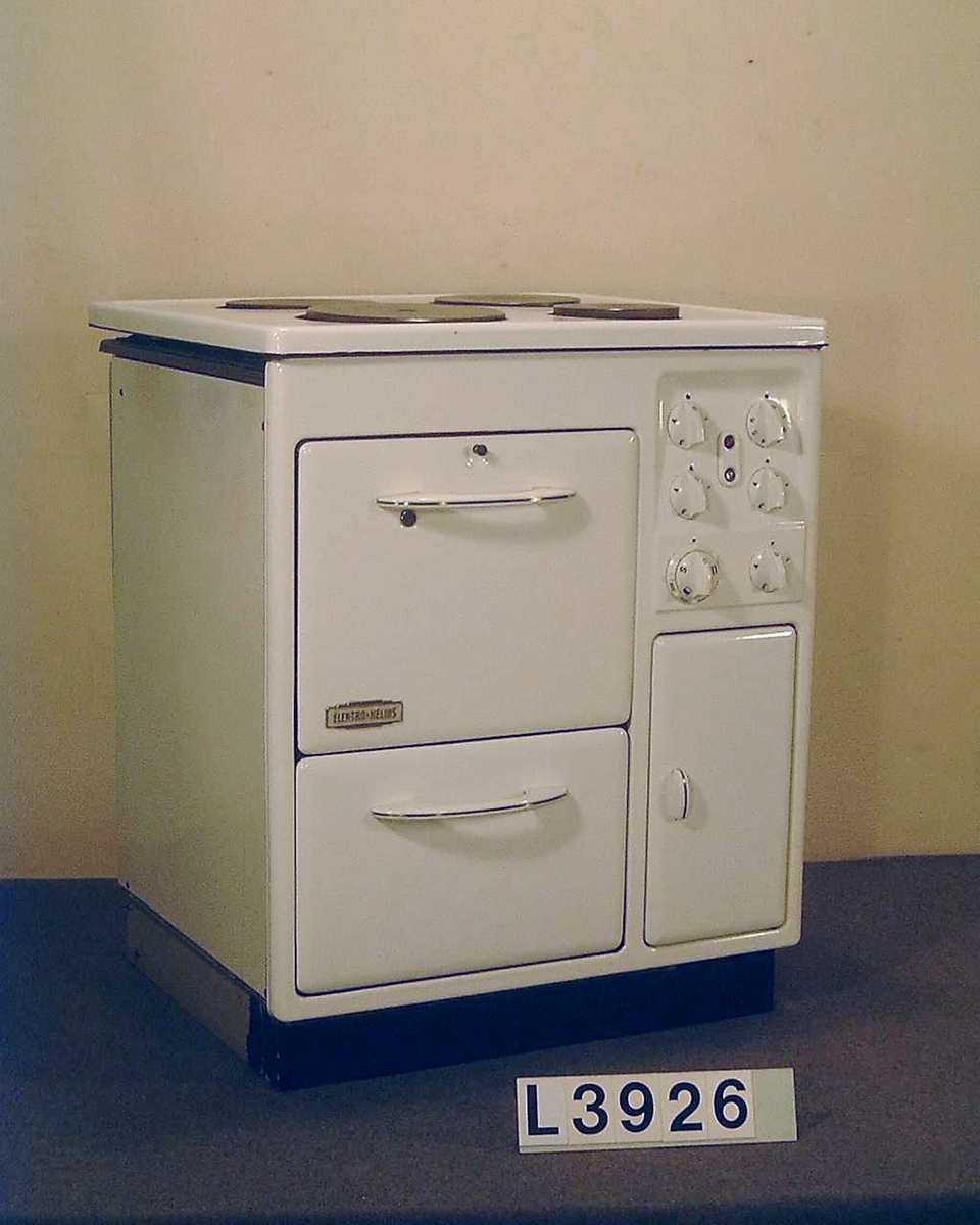 Spis med fyra plattor, ugn och värmeskåp. Överhäll och framsida är emaljerade, övrigt lakerad i benvit färg. Framsidan är heldragen, d.v.s. utan skarvar. Manöverorganen är koncentrerade till ett ställe på framsidan så att de blir lätt synliga uppifrån. Vred och luckhandtag av vit pressmassa. Överhällen är uppfällbar. Spisen står på en grålakerad socke som är försedd med hjul baktill. Alla plåtar finns.