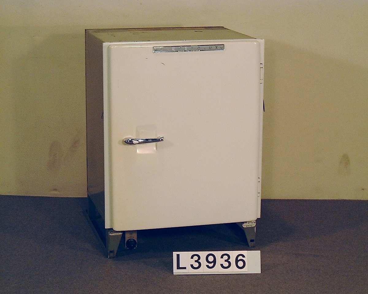 Värmedrivet inbyggnadskylskåp. Fronluckan är benvit och har det klassiska tryckknappshandtaget. Övre och undre ventilgaller saknas.