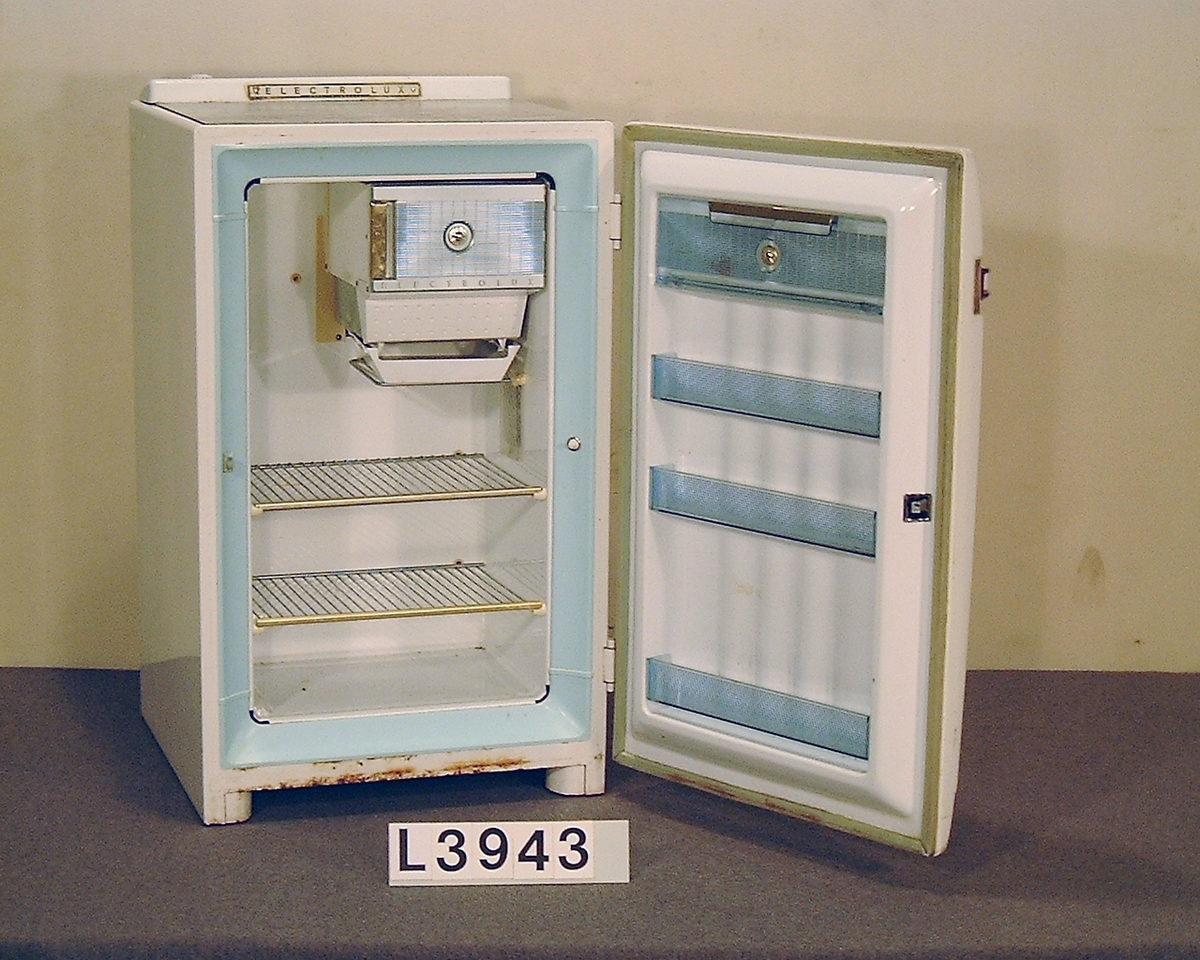 Table Top kylskåp värmedrivet av modell Golden Lux. På fronten löper ett band i gulmetall och handtaget är kromtat. Ovan på skåpet finns en linoleum skiva i gråspräckligt mönster. Kylskåpet har en volym på 110 liter.