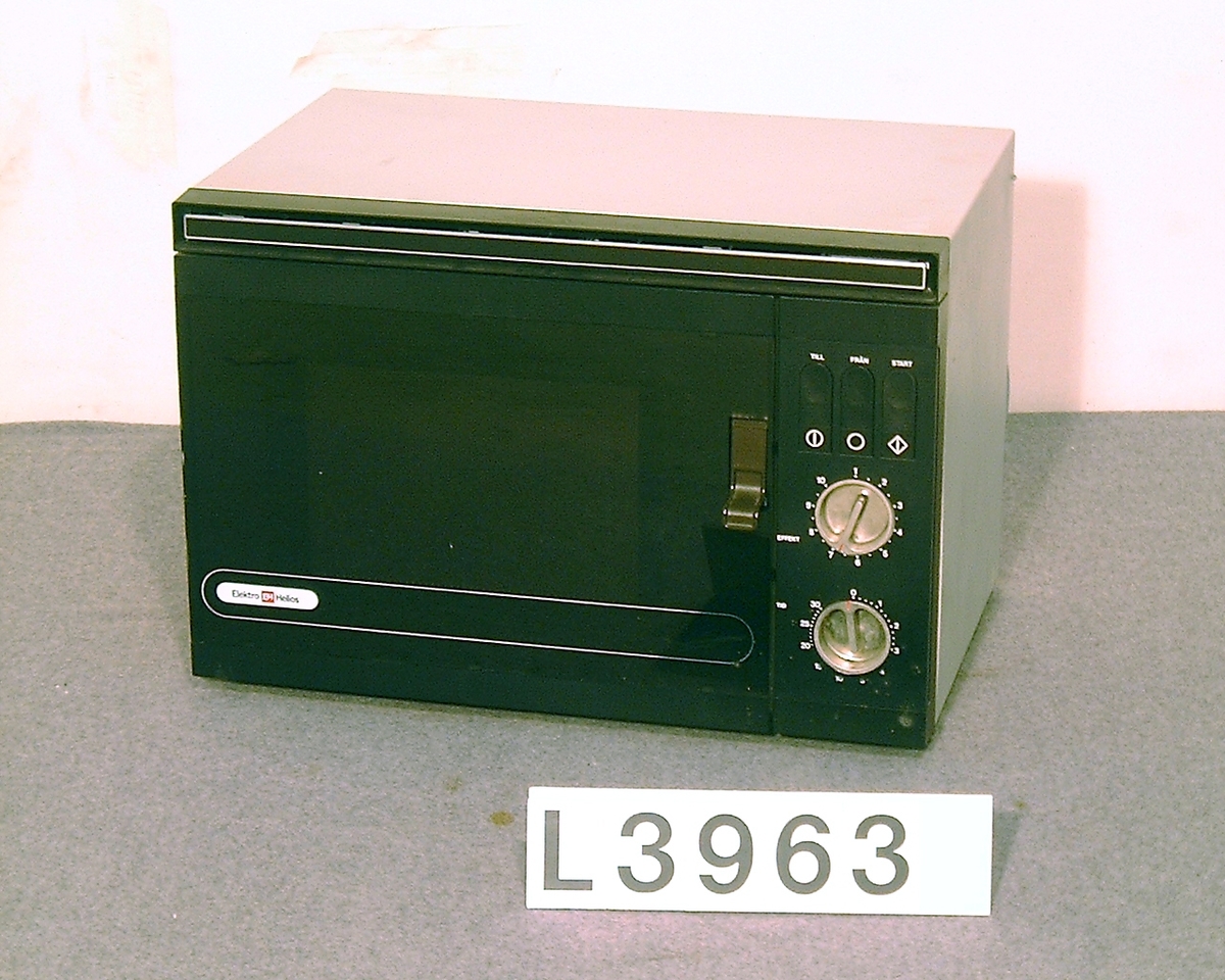 Mikrovågsugn med brun front av märket Elektro Helios. Infällda vred i blank metall för tid och effekt. Infällda tryckknappar för start, samt on & off.