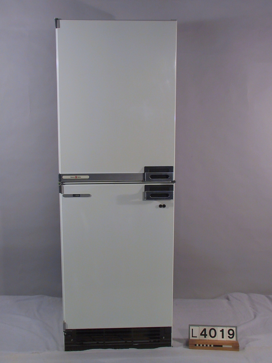 Kombinationsskåp Elektro-Helios med dubbla kompressorer, ett för kyldelen och ett för frysdelen. Kylskåpet är vitt med handtag inspirerade från bilindustrin. Inredningen är vit och dörr- insidorna går i gult.