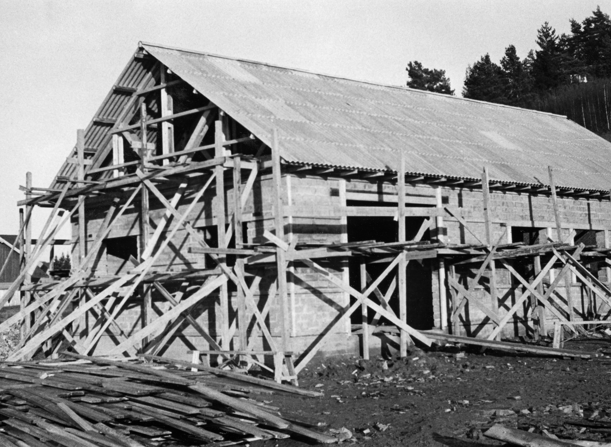 Glomma fellesfløtingsforenings verkstedbygning på Furuholmen i Varteig, fotografert mens den ennå var uferdig, i november 1953.  Fotografiet viser eksteriøret, der veggene var murt av såkalte «tretong-blokker» på fundamenter av betong.  Da dette fotografiet ble tatt sto det fortsatt stillas rundt veggene, dører og vinduer var ennå ikke innsatte, og røstet var fortsatt åpent.  Taket var nettopp lagt med bølgeplater – antakelig av eternitt – som tekkingsmateriale.  I forgrunnen til venstre lå en haug med forskalingsbord.  

Bygginga av det nye verkstedet var ett av flere tiltak som ble gjort som forberedelse til at en rekke funksjoner skulle flyttes fra det gamle fløtingssenteret ved Nes til Furuholmen.  Dette ble gjort fordi Furuholmen lå like ved Glennetangen, der hovedlensa for denne delen av vassdraget hadde ligget siden siste halvdel av 1930-åra.  Flyttinga av så vel funksjonærer som tekniske servicefunksjoner ble sluttført i 1958-59.