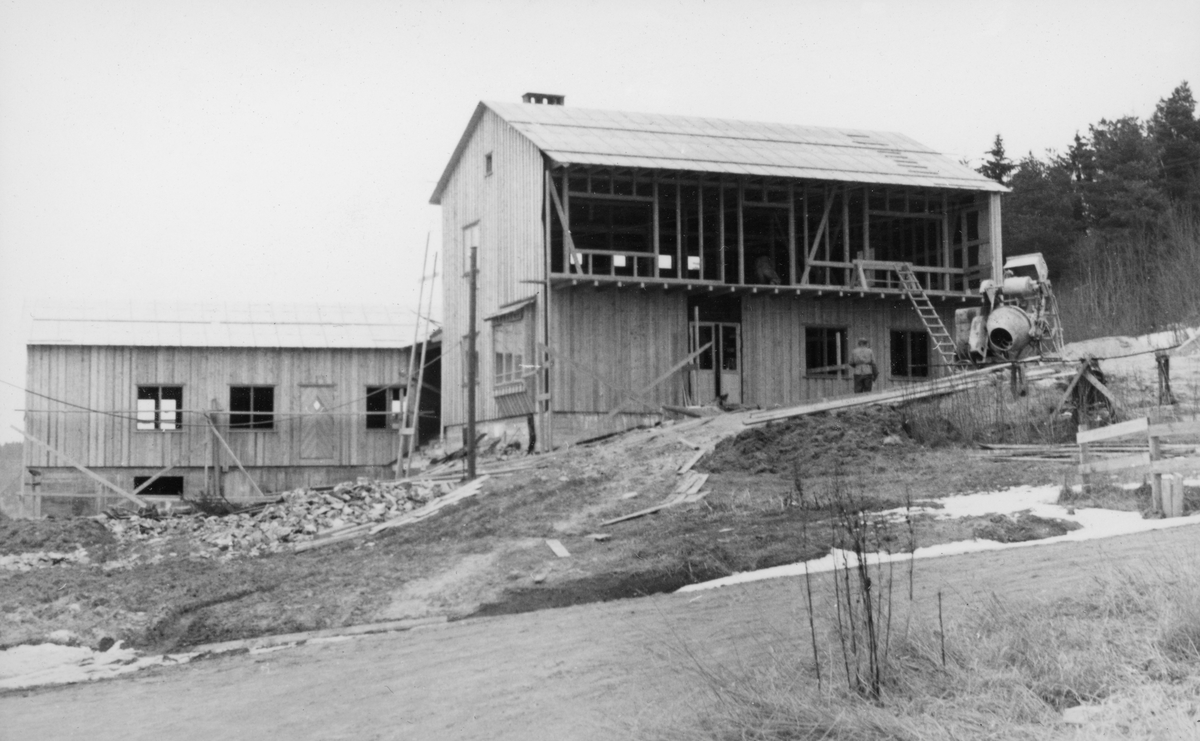 Bestyrerbolig og kontorfløy under oppføring på Glomma fellesfløtingsforenings eiendom Furuholmen i Varteig vinteren 1955.  Fotografiet er tatt sørfra, mot bygningene, som begge var kommet under tak.  Boligdelen, til høyre, hadde fått bordkledning på gavlveggen mot vest og i første etasje på langveggen mot sør.  I andre etasje derimot, hvor det var lagt til rette for en langsgående veranda, var det derimot ikke påsatt noen bordkledning.  På gardsplassen, ved boligens sørøstre hjørne, sto fortsatt sementblanderen som var brukt i forbindelse med byggearbeidet.  På kontorfløyen (til venstre) sto stillaset etter panelingsarbeidet fortsatt. 

Reisinga av nye boliger, verkstedanlegg og kai ved Furuholmen var ledd i et arbeid for å kunne flytte virksomhet fra det gamle fløtingssenteret ved Nes, cirka to mil høyere opp i vassdraget, til Furuholmen.  Dette ble gjort fordi Furuholmen lå like ved Glennetangen, der hovedlensa for denne delen av vassdraget hadde ligget siden siste halvdel av 1930-åra.  Flyttinga av så vel funksjonærer som tekniske servicefunksjoner ble sluttført i 1958-59.  Etter at tømmerfløtinga i Glomma ble avviklet i 1985, ble anlegget solgt til nye eiere.  Deretter den avbildete bygningen brukt som restaurant ei stund. 
