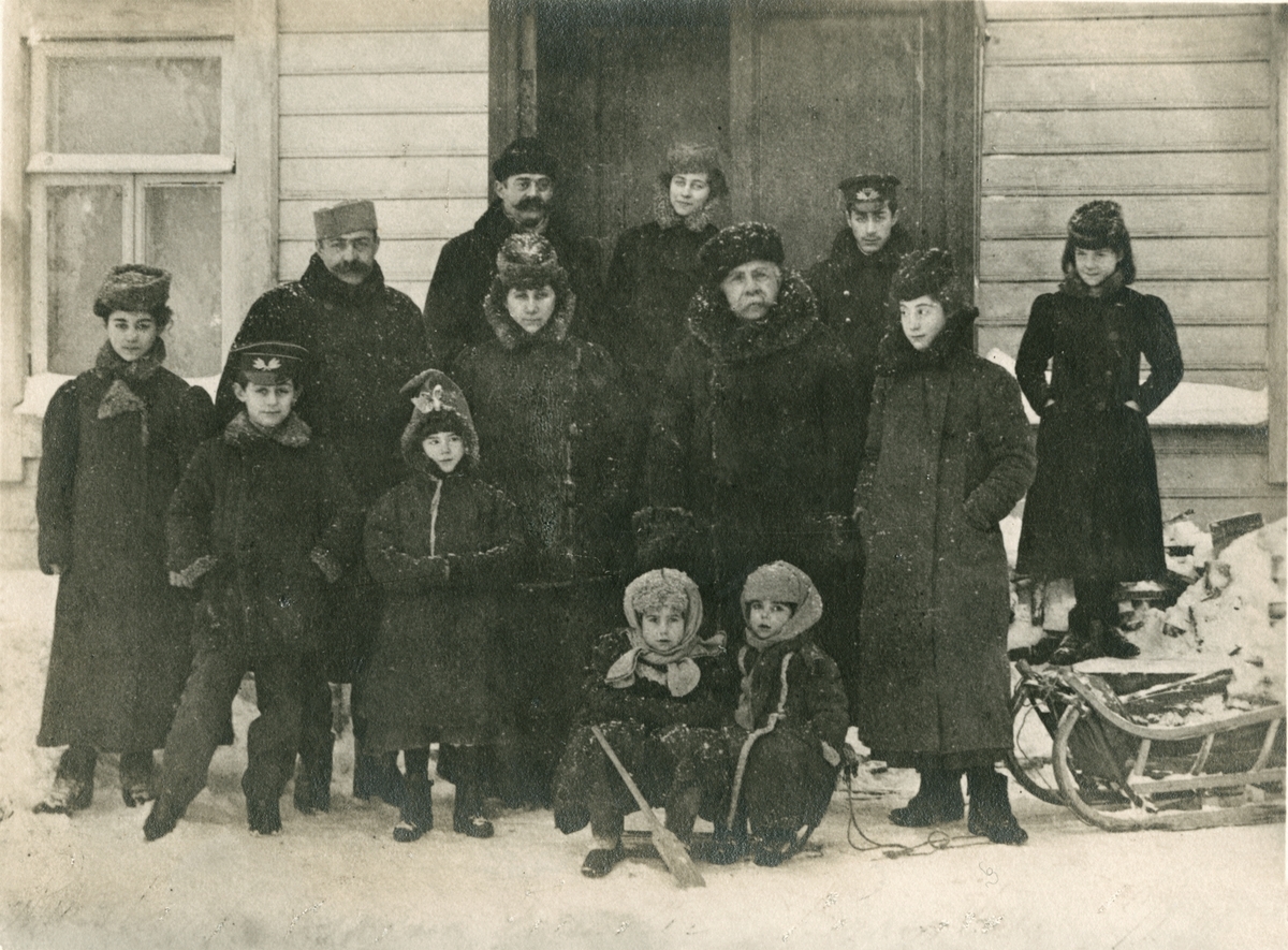 Familien Rostin poserende foran et hus i Borovichi, nyttårsdag 1903. Bakerst fra venstre: Onkel Helidor Rostin, Florentine, Teodor, Julie. Midten fra venstre: Elisabeth, Michail, Sophia, farfar Adolph, Valentine. Foran fra venstre: Ignazy, Victoria, Serafima, Nikolaj.