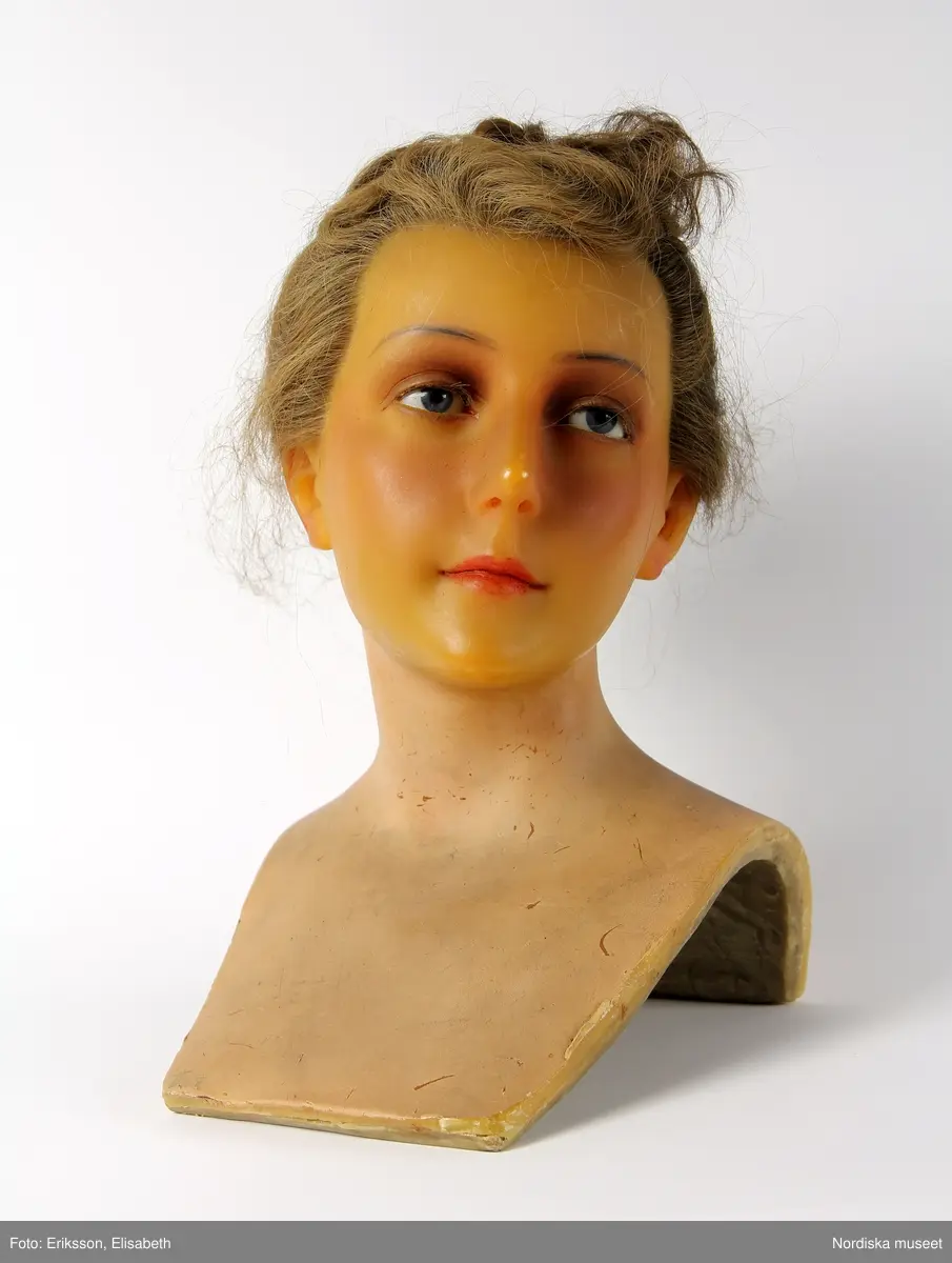 Skyltdockshuvud, kvinna, av vax med riktigt hår, ögonfransar och ögon av glas. Med hals och övre del av torso. På baksidan av torso text "Paul Baschwitz / Berlin C". Håret friserat i 1940-tals frisyr (hårnålar ingår ej i förvärvet).
Anm. spricka vid vänster öga och vax gulnat.
/Helen Persson 2018-02-13