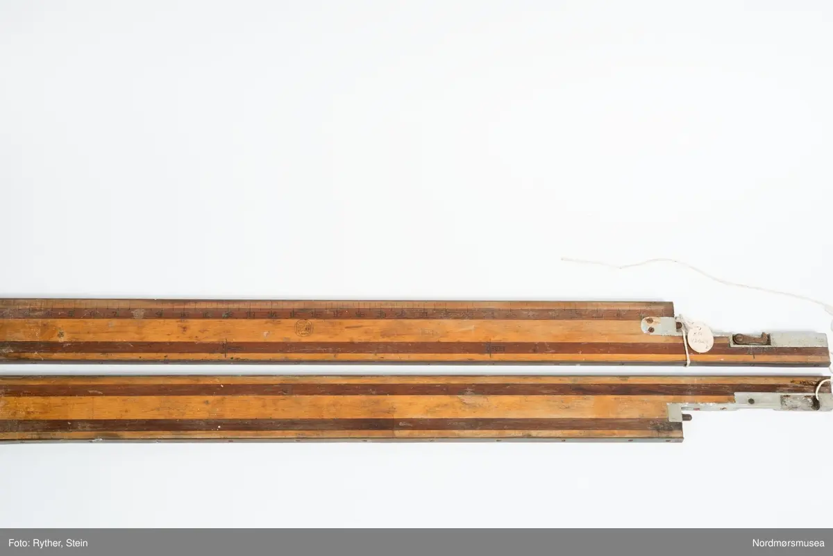 Linjalen er på 72 inches = 6 feet. Oppmerkningen slått inn med stempler. Delt ved 32 1/2" - 39 1/2". Her er satt på et aluminiumsbeslag emd tappesystem og krok. Tallene er stemplet på ei stripe av brunt tre, resten er lyst treverk. Messingskinner skrudd til over- og undersiden av linjalen.