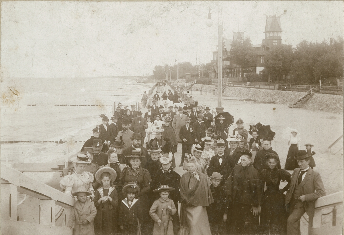 Fotografi av en eller annen tilstelning på strandpromenaden i Kranz, nå Zelenogradsk. I forreste rekke står Valentine og Ignazy Rostin som nr. 2 og 3 fra venstre. Øvrige personer er ukjente. Bak sees Kranz damebad med det karakteristiske høye tårnet. Familien Rostin ferierte ofte i Kranz, og Victoria ble født der, antagelig 1897. 

Bildet er tatt 12.sept 1897.