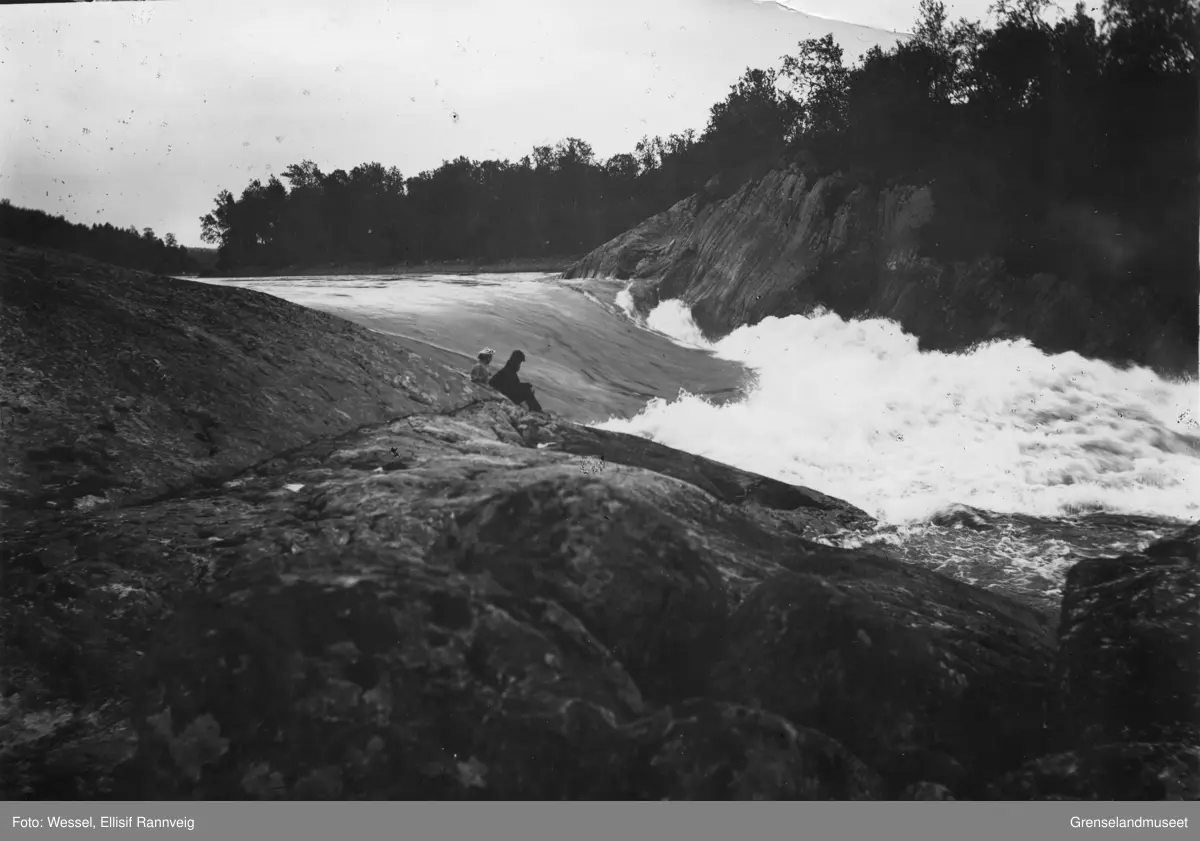 Harefoss i Pasvik. Et par sitter ved elvekanten og ser utover fossen.
