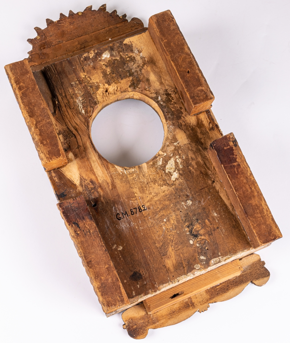 Klockfodral i skuret trä, blåmålat och förgyllt. Reliefbilder; krona, fiskar, delfiner, växtornament samt svårlästa bokstäver (Carl Johans namnschiffer?) samt märkt 1812. Runt hål i mitten.