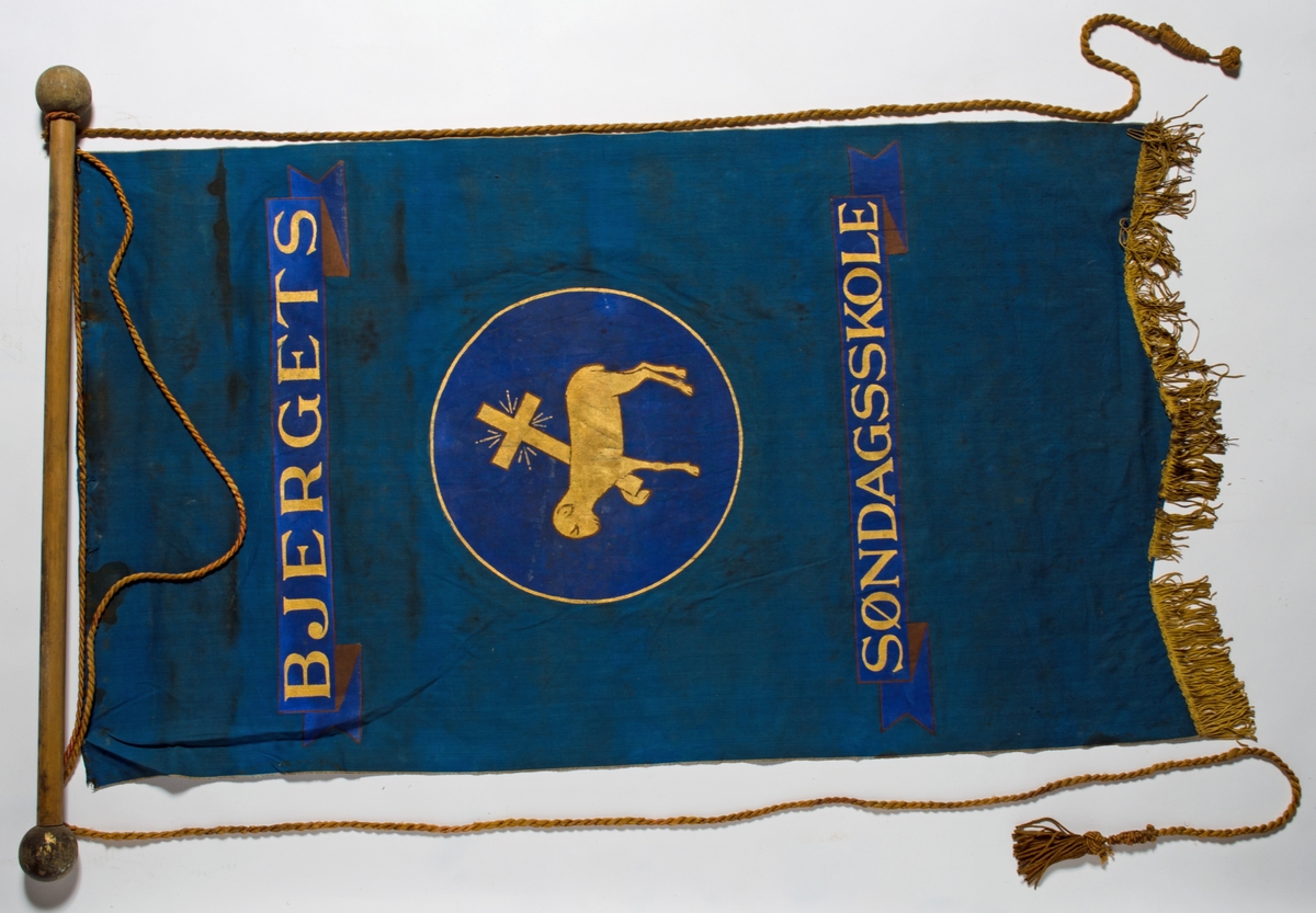 Blå faneduk i bomullslerret med tre korte tunger kantet med frynser nederst. Motiv, påskrift og frynser i gull. 

Framside: Sentrert motiv av Guds lam som bærer korset i sirkel.
Bakside: Sentrert motiv av Guds lam som bærer korset i sirkel.