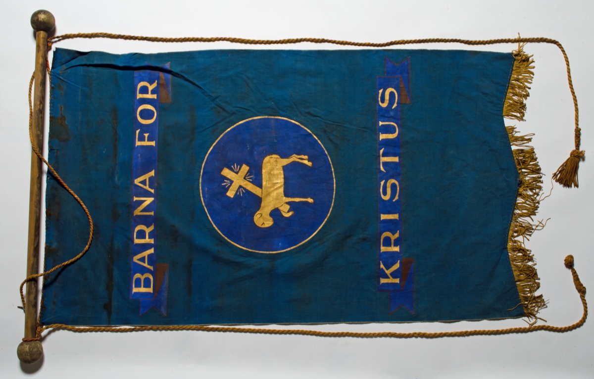 Blå faneduk i bomullslerret med tre korte tunger kantet med frynser nederst. Motiv, påskrift og frynser i gull. 

Framside: Sentrert motiv av Guds lam som bærer korset i sirkel.
Bakside: Sentrert motiv av Guds lam som bærer korset i sirkel.