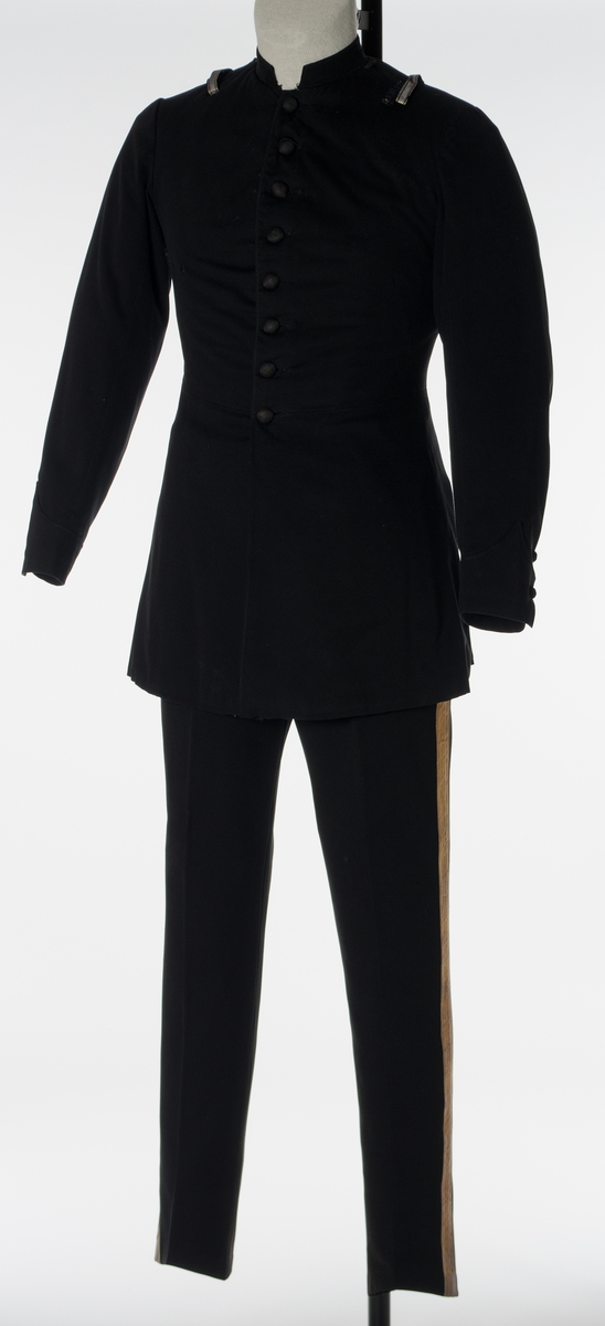 Enkeltspent jakke til uniform i sort ull. Åtte tekstiltrukne knapper i fronten. Kraven er opprettstående og kan lukkes med en metallhekte.  Skuldrene har påsydd hempe på hver side av kragen og hver skulder er dekorert med et 9,5 cm langt vevd, sølvbånd, festet i hver ende vertikalt på skulderen. Baksiden har splitt opp til livlinjen med lommer på hver side inn fra splitten og tre par tekstiltrukne knapper. Nederst på ermene er det utenpåsydd mansjett med spiss og to tekstiltrukne. Innvendig er jakken helforet med sort bomullsfor og vattering i overdelen. Gult fôr i ermene. Opphengshemper i nakken. 

Bukse i mørk blå ull med to lommer bak. Vevd gullbånd i sidene. Gylf lukkes med metallhekte og fire knapper (ant. i tre). Åtte metallknapper utvendig på linning. Hvitt fôr med smale striper i rødt, lyseblått og lysegrått i linning. Sandfarget fôr i lommene.