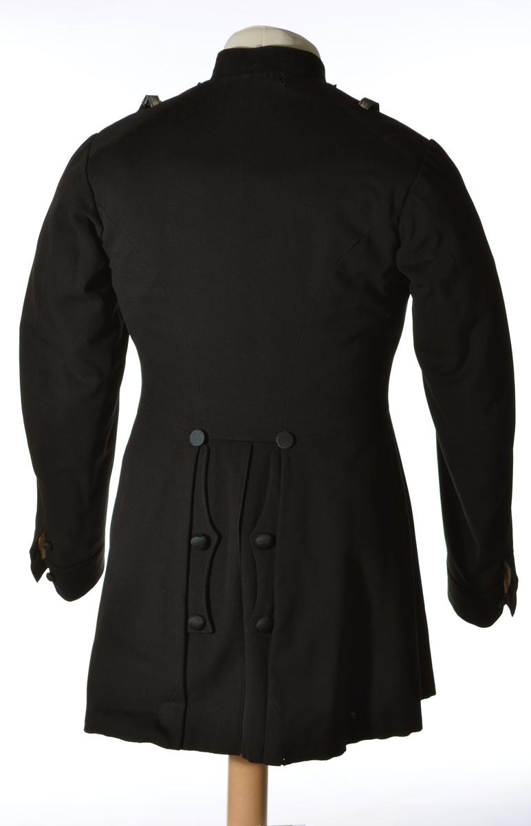 Enkeltspent jakke til uniform i sort ull. Åtte tekstiltrukne knapper i fronten. Kraven er opprettstående og kan lukkes med en metallhekte.  Skuldrene har påsydd hempe på hver side av kragen og hver skulder er dekorert med et 9,5 cm langt vevd, sølvbånd, festet i hver ende vertikalt på skulderen. Baksiden har splitt opp til livlinjen med lommer på hver side inn fra splitten og tre par tekstiltrukne knapper. Nederst på ermene er det utenpåsydd mansjett med spiss og to tekstiltrukne. Innvendig er jakken helforet med sort bomullsfor og vattering i overdelen. Gult fôr i ermene. Opphengshemper i nakken. 

Bukse i mørk blå ull med to lommer bak. Vevd gullbånd i sidene. Gylf lukkes med metallhekte og fire knapper (ant. i tre). Åtte metallknapper utvendig på linning. Hvitt fôr med smale striper i rødt, lyseblått og lysegrått i linning. Sandfarget fôr i lommene.
