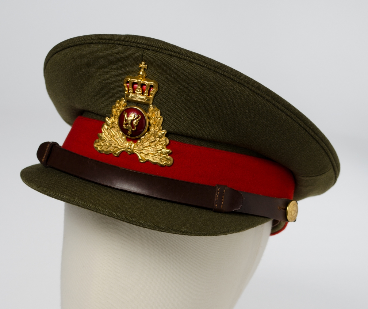 Militærgrønn lue i ullstoff. Stofftrukket lueskygge. Rødt ullbånd og lærrem i front festet med gullfarget knapp, dekorert med kryss omkranset av løvkrans, på hver side. Distinksjon/emblem i front med ekeløv, knapp med den norske løve og krone over. Föret med burgunderrødt syntetisk fôr. Svetterem i lær og plastbeskyttelse i pullen.