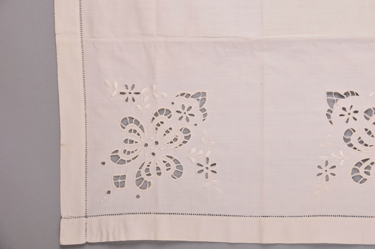 Kvadratisk duk med broderi i kvart hjørne.Duken er i bomull, og har holbroderi, engelsk broderi, plattsum, stilkesting m.m. Kring kanten er der ein holfald. Falden er relativt brei. Bak på kanten av duken er der skrive med blyant: " Sauma av Anne Lidtveit Oftelid (født 1998 i Kvitseid)