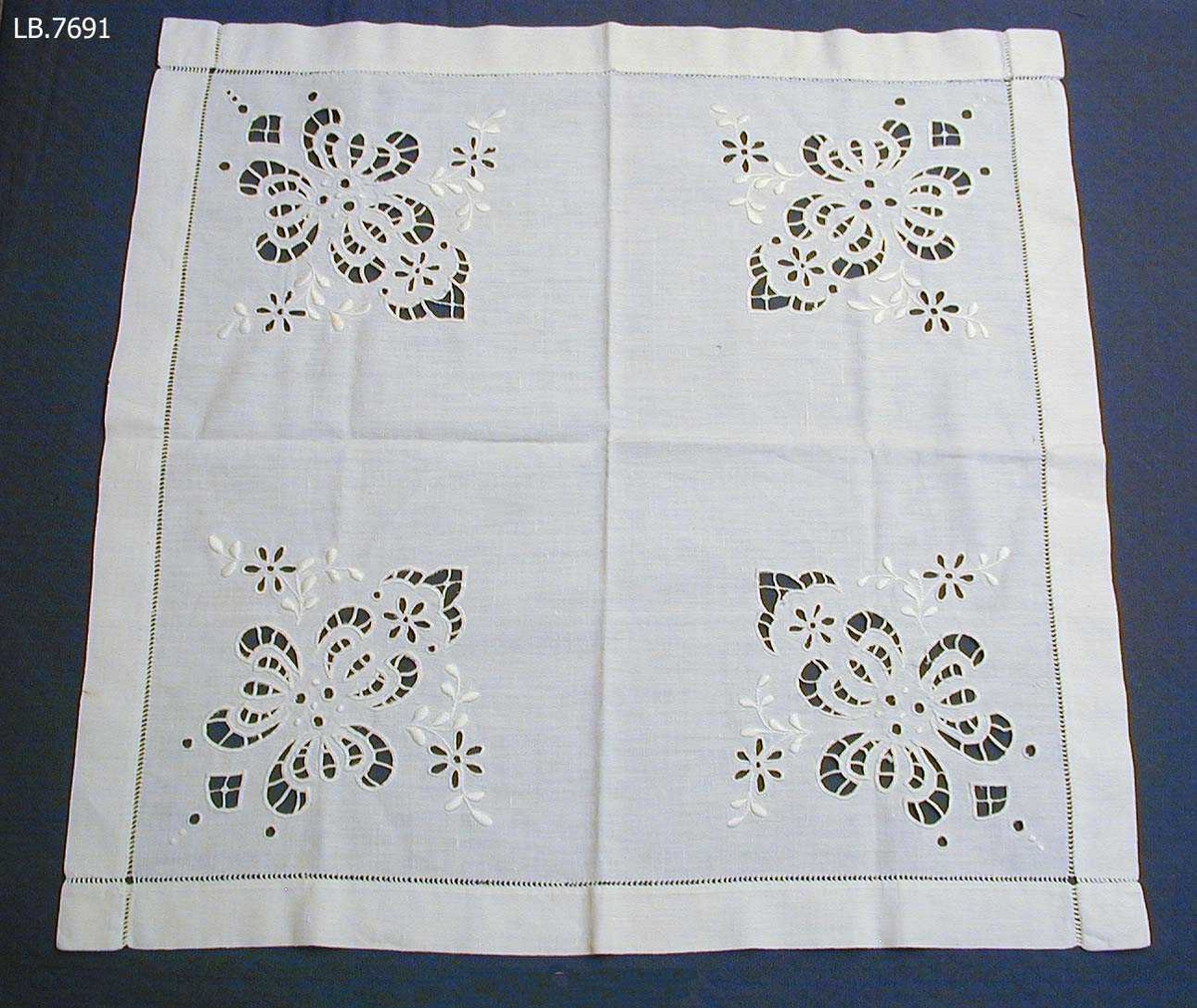 Kvadratisk duk med broderi i kvart hjørne.Duken er i bomull, og har holbroderi, engelsk broderi, plattsum, stilkesting m.m. Kring kanten er der ein holfald. Falden er relativt brei. Bak på kanten av duken er der skrive med blyant: " Sauma av Anne Lidtveit Oftelid (født 1998 i Kvitseid)