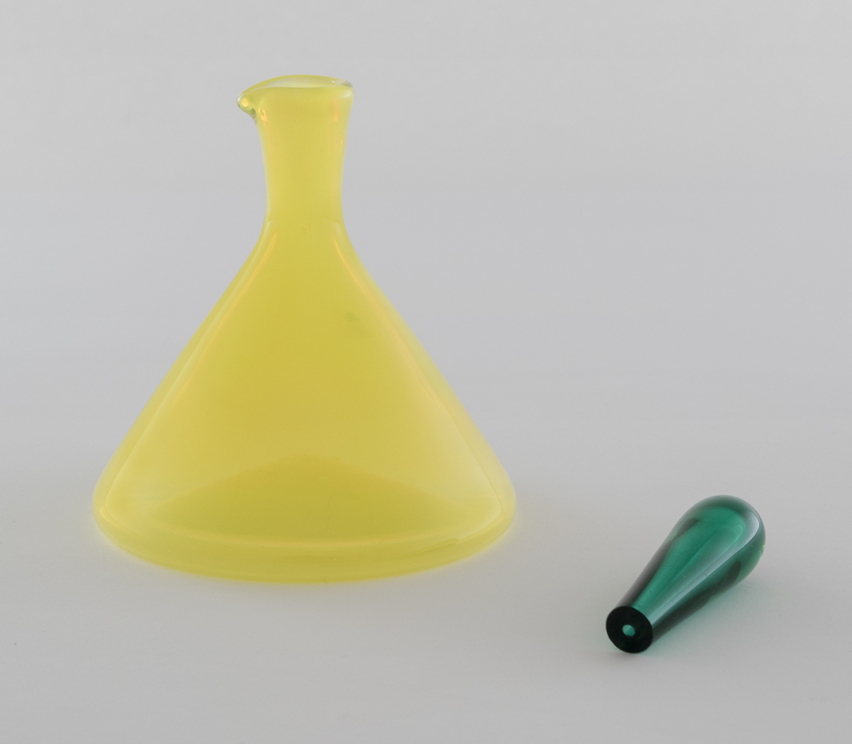 Edikk- eller oljekaraffel med propp i farget glass. Konisk koprus i halvgjennomskinnelig gulfarget glass, som avsluttes i en smal hals med tut. Den dråpeformede proppen er utført i gjennomskinnelig grønnfarget glass.