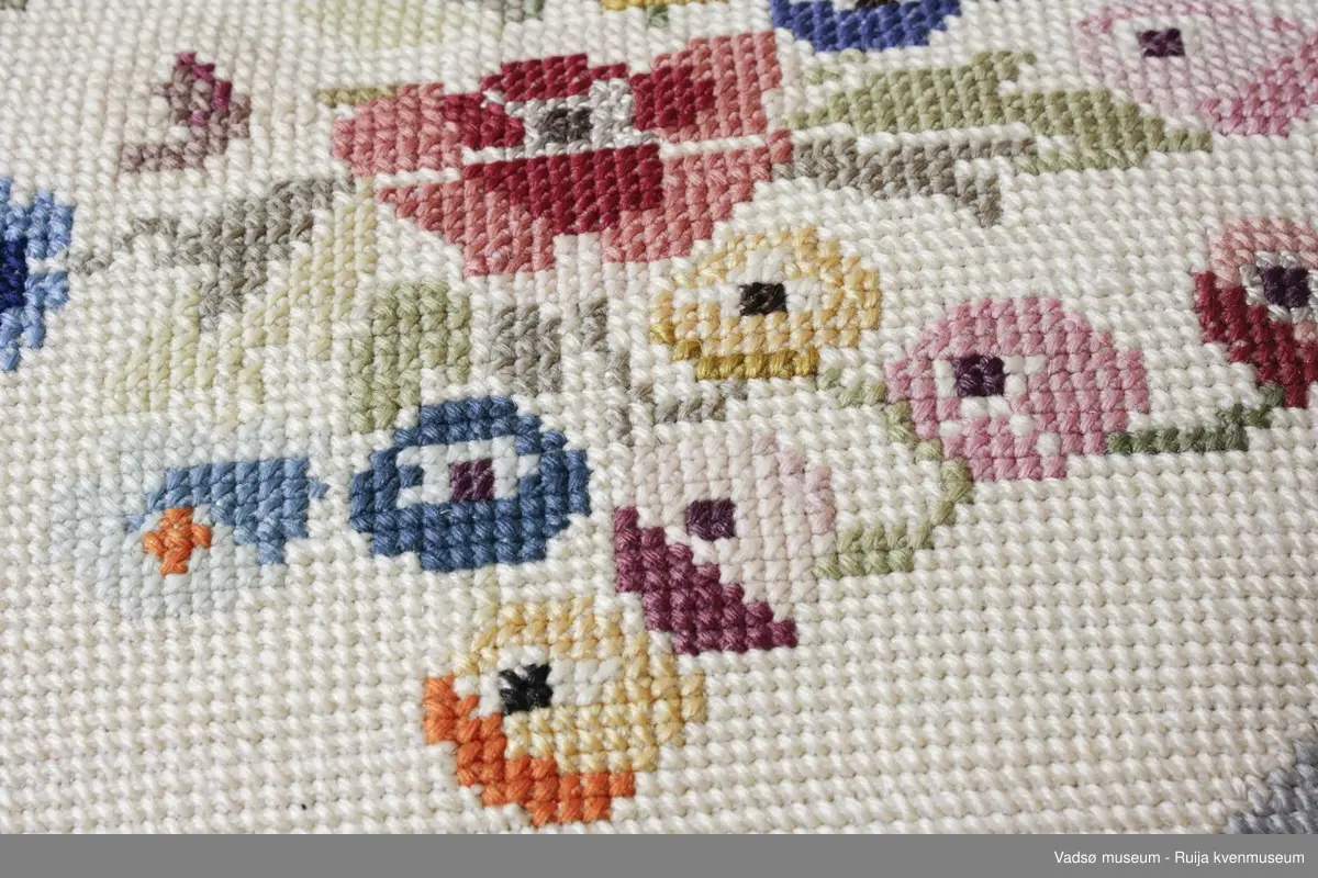 1 stk pute. Tidl. reg. brodert korssting på tysk sekk.Fra ca. 1942-43
Blomstermotiv i midten, striper diagonalt i hjørnene. Strikket grønn bakside.