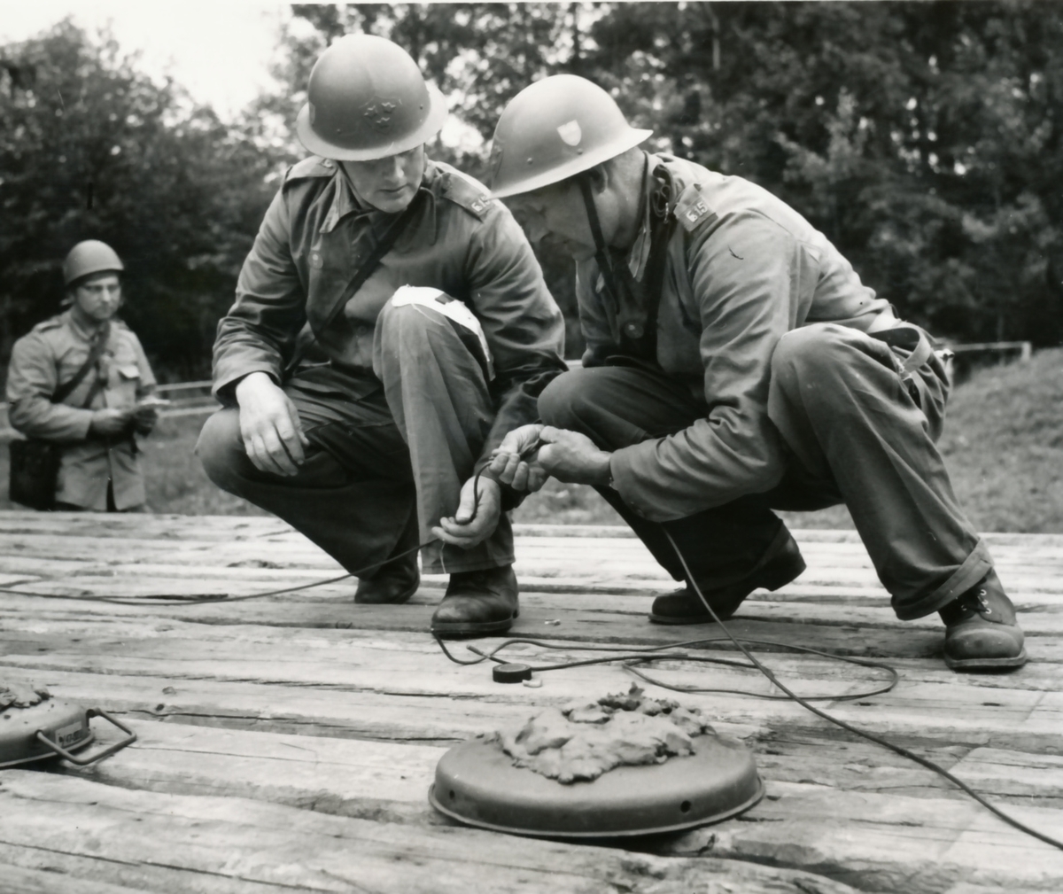 Rikshemvärnstävlingen 1967, sid 14 och 15

Min- och sprängtjänst.
Gruppen förbereder sprängning av en träbro med stridsvagnsminor. Minorna tänds med Sprängdeg och Pentylstubin.

Bild 1. Lag 105, TV Karlstad utför en korrekt 90-graders skarv på ringledning av Pentylstubin.

Bild 2. Lag 13, Hallabro, Fo 15. Gunnar Augustson och Per Pettersson.

Bild 3 och 4. Från samma stn.