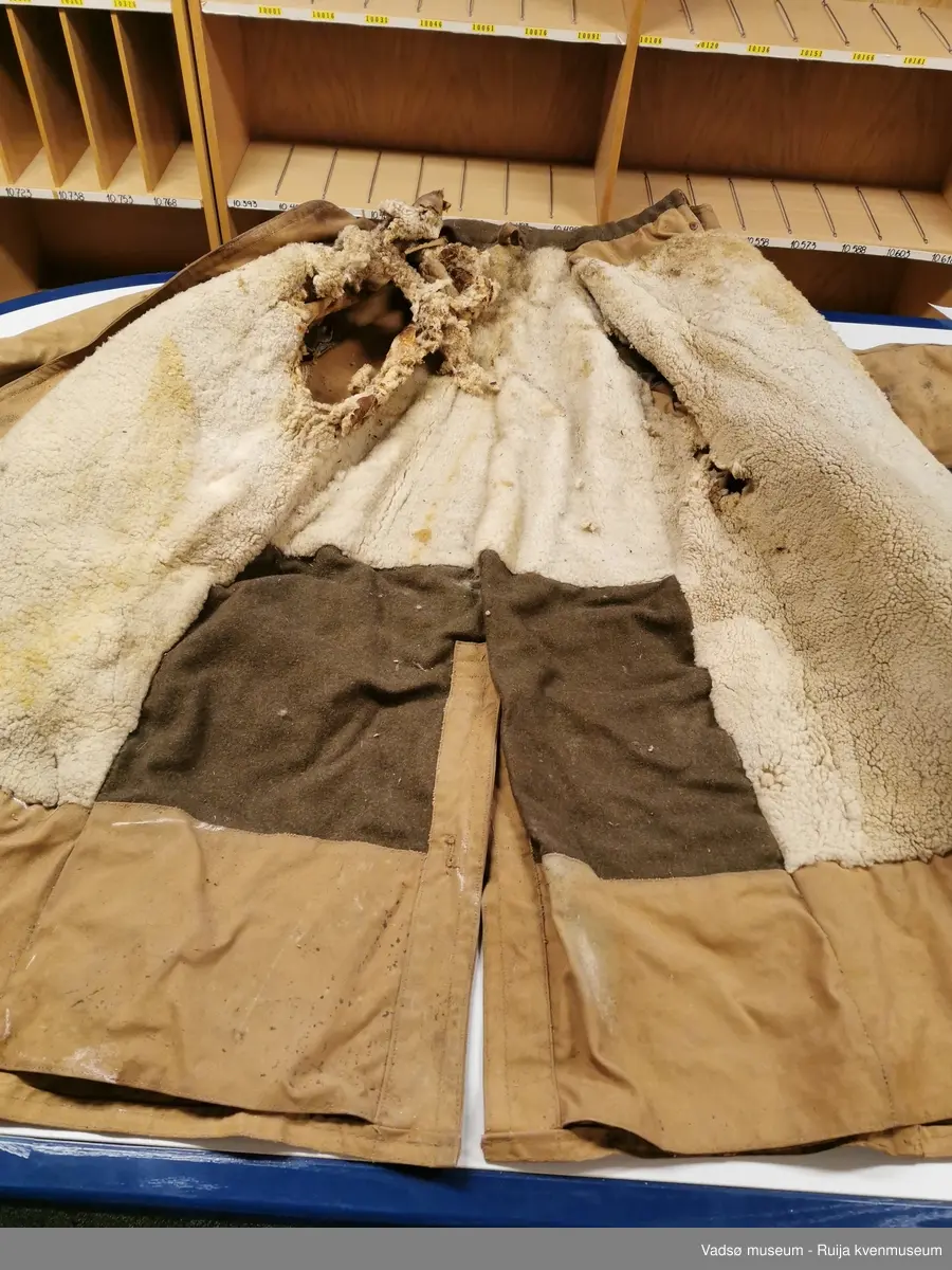 Lerretstoff med saueskinn inni. Nokså slitt, store hull i ullforet og under armene på jakken.